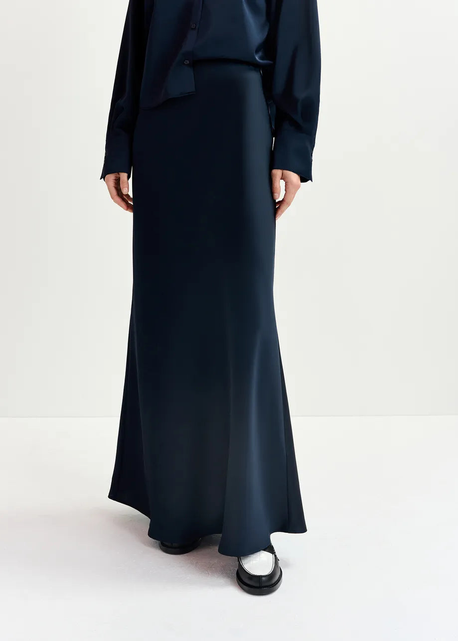 Person wearing the Essentiel Antwerp Giada Satin Maxi Skirt in navy and a matching dark blue top, with white shoes visible at the bottom.