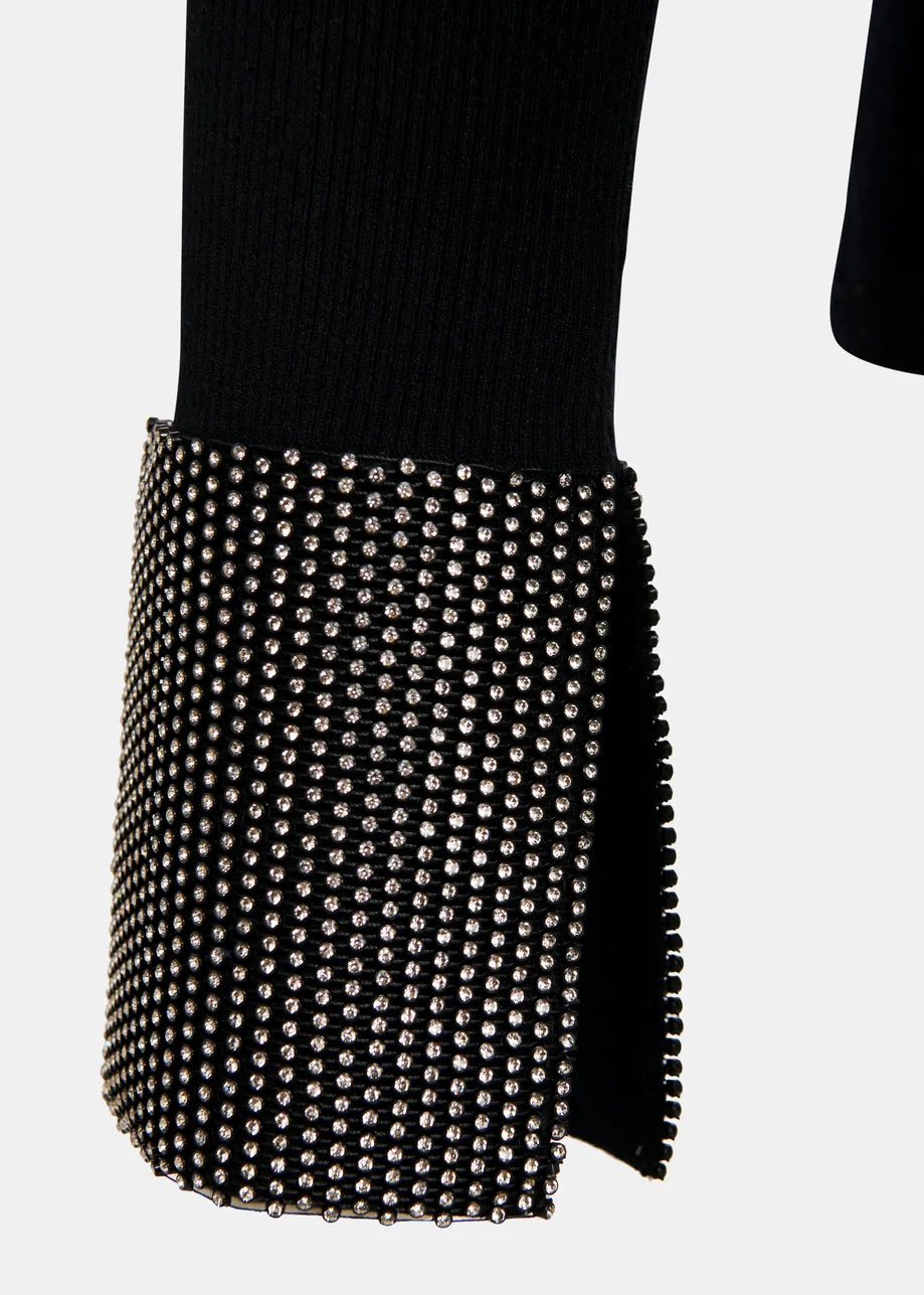 A close-up of the Gomi Rib-knit Sweater - Black by Essentiel Antwerp, showcasing its wide, rhinestone-embellished cuff adorned with rows of small silver studs, set against a plain background.