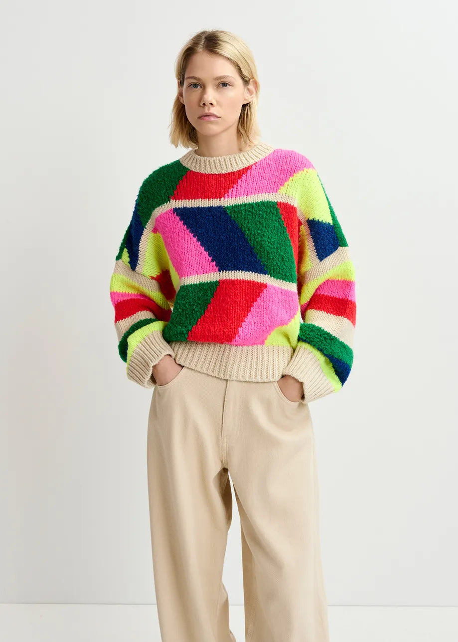 A person stands against a plain background, wearing the Gradation Knit Sweater - Multicolour by Essentiel Antwerp and beige pants, looking straight ahead with hands in pockets.