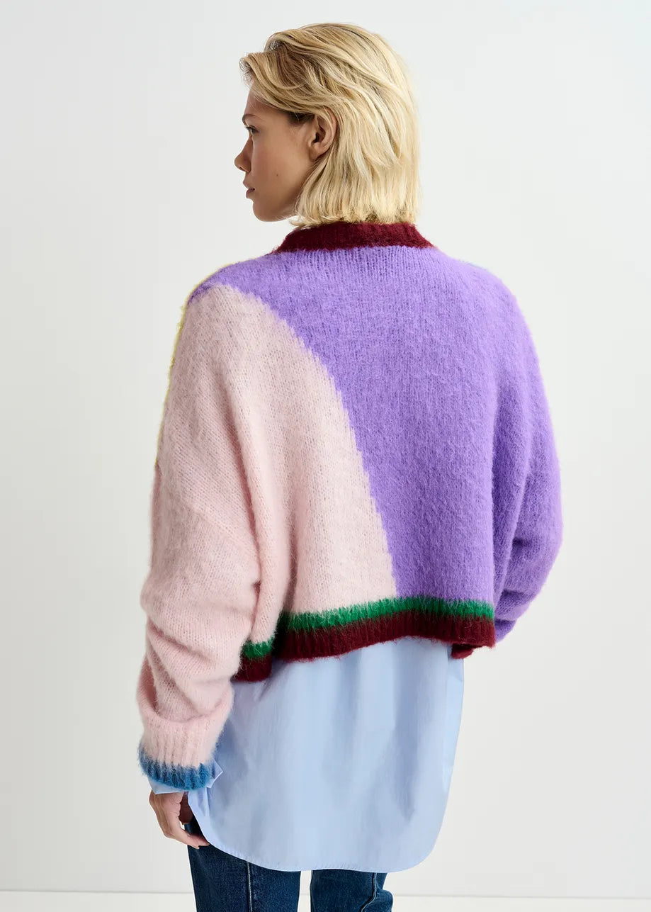 A person with short blonde hair is wearing the Essentiel Antwerp Groupie Knit Sweater in multicolour, featuring a pastel-colored, long-sleeve fuzzy texture with an abstract intarsia-knitted design over a light blue shirt. They are facing away from the camera.