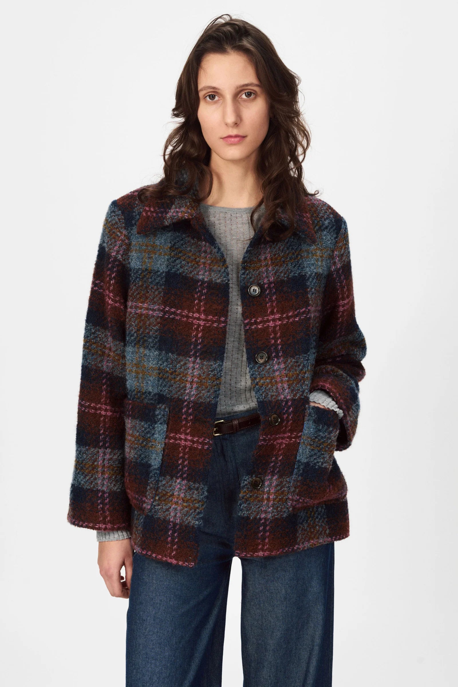 A woman wears a Nué Notes Glasgow Jacket - Fall Multi Check, styled oversized over a gray top and blue jeans, standing against a plain white background.