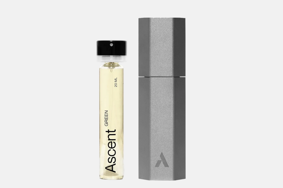 A glass vial of green perfume extract from the Ascent Starter Pack - Green next to its tall, hexagonal grey case.