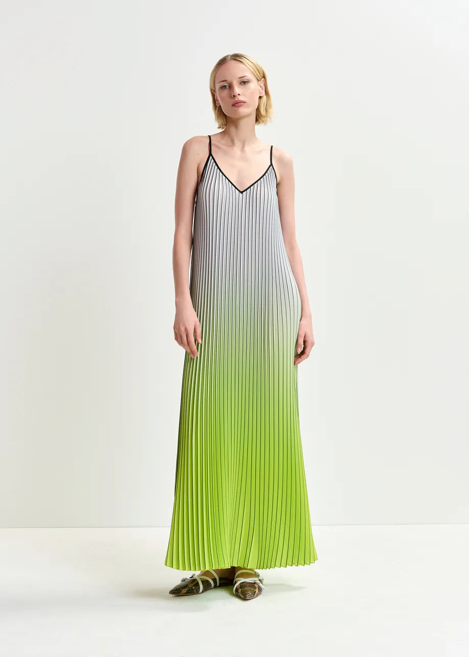 A woman in Essentiel Antwerp's Haurus Gradient Slip Dress - Green, made of recycled polyester with a stunning white-to-green gradient and black lines, stands against a plain background, highlighted by her flat shoes.