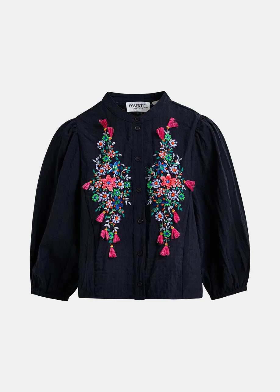 The Heartfelt Shirt by Essentiel Antwerp is a navy blouse with puffed sleeves, a mandarin collar, colorful floral embroidery, and tassels on the front.