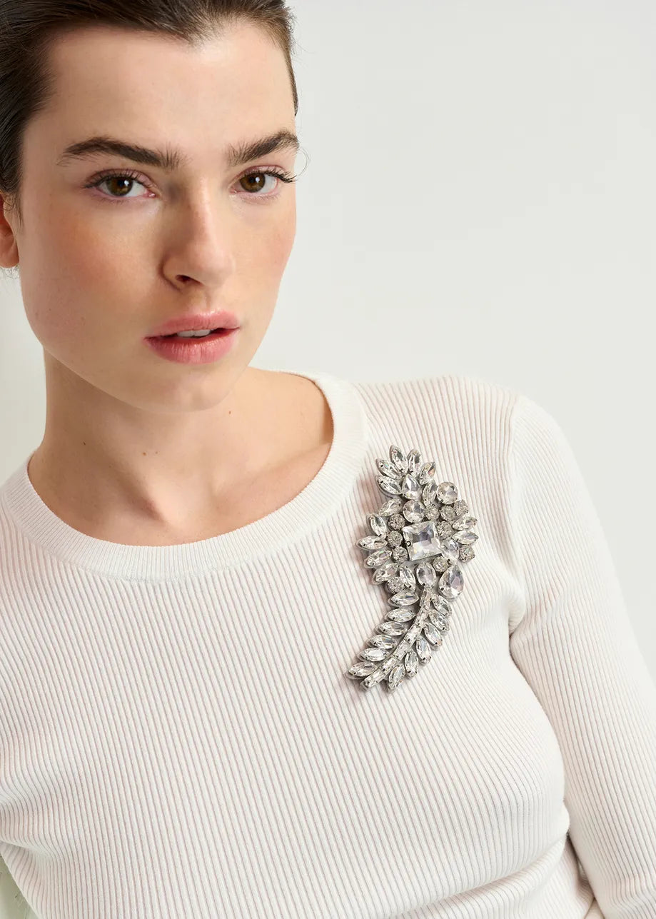 A person in a white ribbed top is adorned with the Essentiel Antwerp Rhinestone Brooch - Silver on their shoulder, featuring shimmering rhinestones that catch the light.