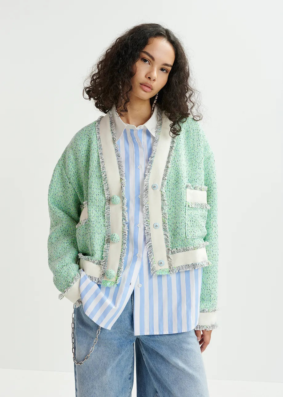 A person wears an oversized green textured cardigan styled as a Hoola Cropped Tweed Cardigan by Essentiel Antwerp over a blue and white striped shirt with light blue jeans, standing against a plain background. This ensemble is a versatile transitional piece for any wardrobe.