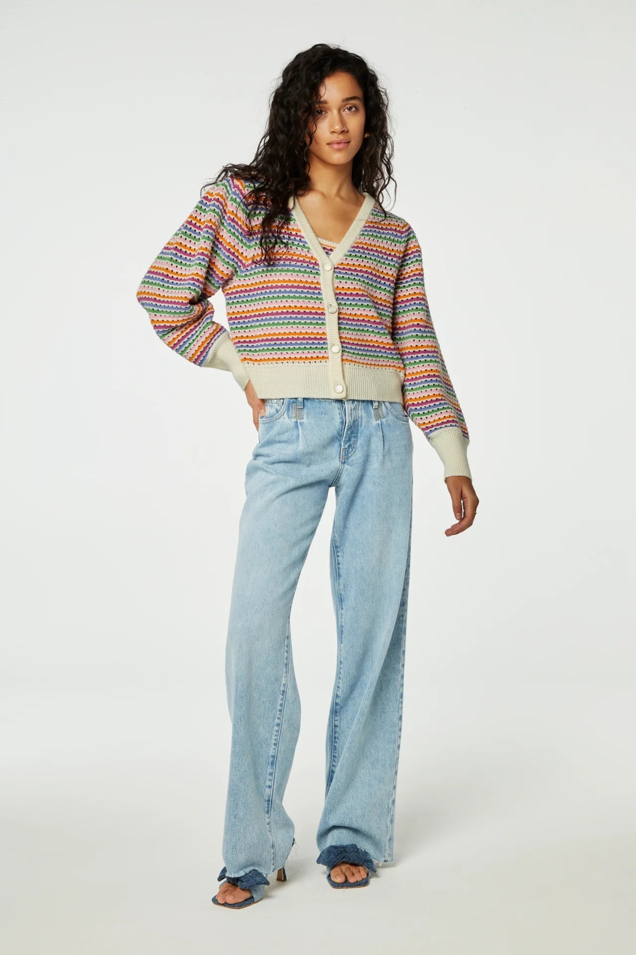 A woman models a colorful striped Fabienne Chapot heather cardigan and blue jeans, standing against a plain background.