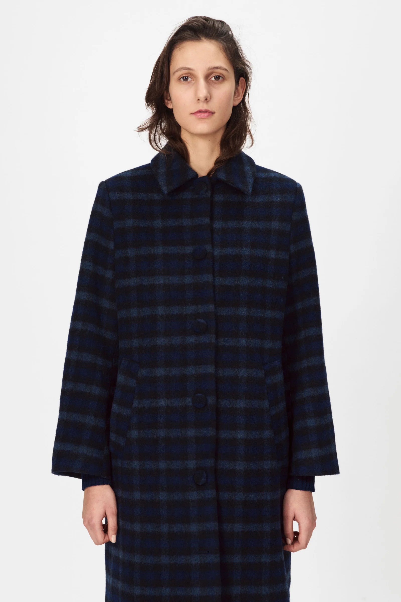 A person models the Nué Notes Helsinki Coat in navy, standing against a white background and highlighting this classic autumn-winter style.