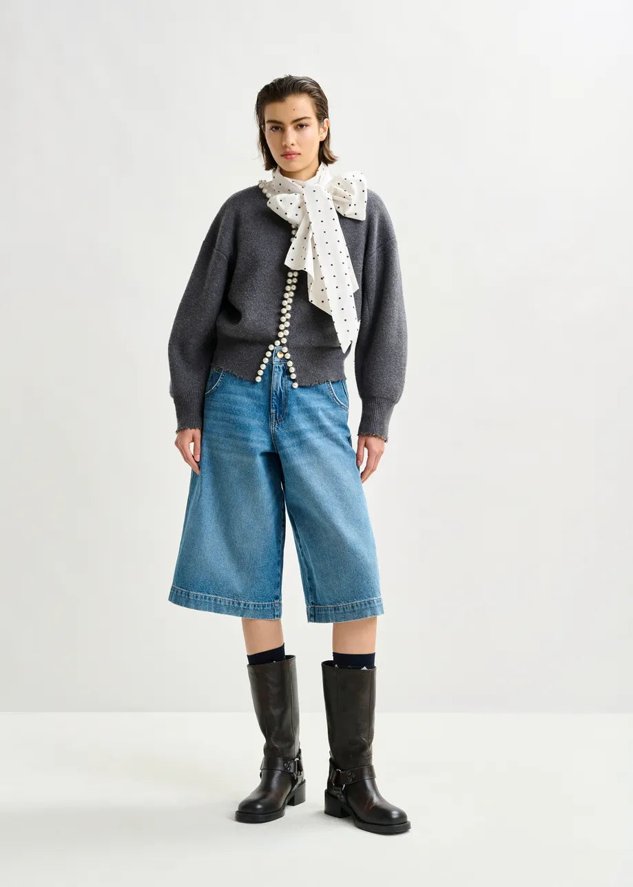 A person wears the Essentiel Antwerp Ideas Pearl-Embellished Cardigan in grey, paired with a white scarf with black dots, wide knee-length denim shorts, and black boots against a plain background.