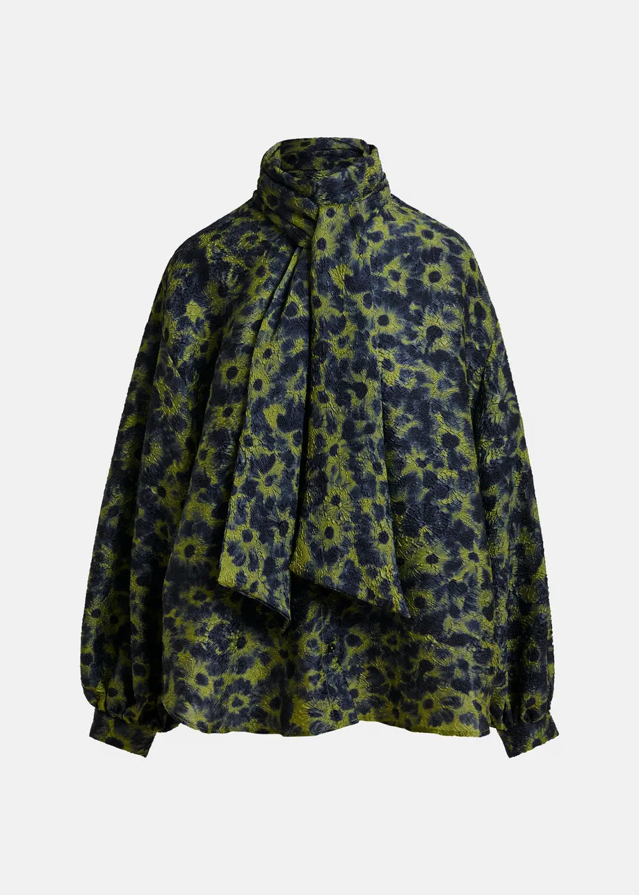 The Essentiel Antwerp Illicium Floral Jacquard Shirt in khaki features long sleeves, a green and black flower pattern, a high neck, and an attached wide pussy-bow scarf tie.