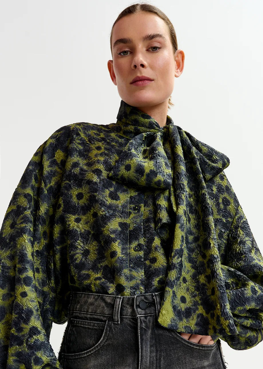 A person wears the Essentiel Antwerp Illicium Floral Jacquard Shirt in khaki with high-waisted black jeans, standing against a plain white background.