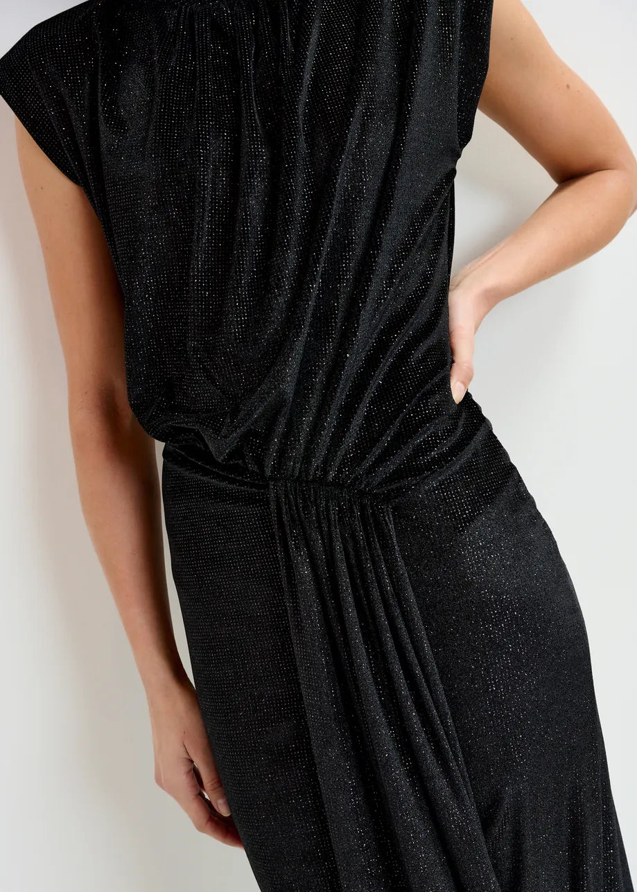 A person wears the Essentiel Antwerp Inche Midi Dress in black, a sleeveless, draped, shimmery stretch-jersey style, standing against a plain background with one hand on their hip.