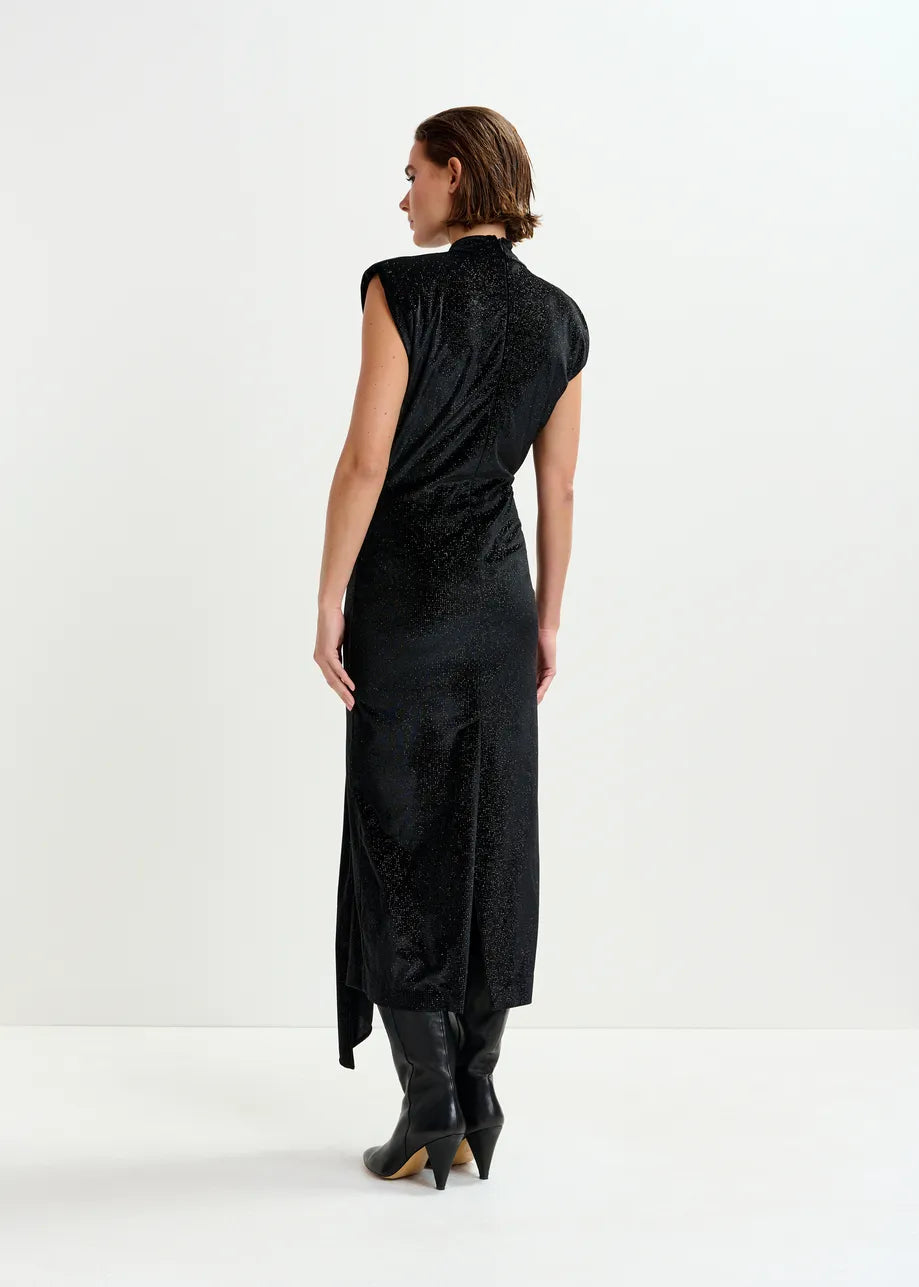 A person stands facing away, wearing the Essentiel Antwerp Inche Midi Dress in black with cap sleeves and black knee-high boots against a plain white background.