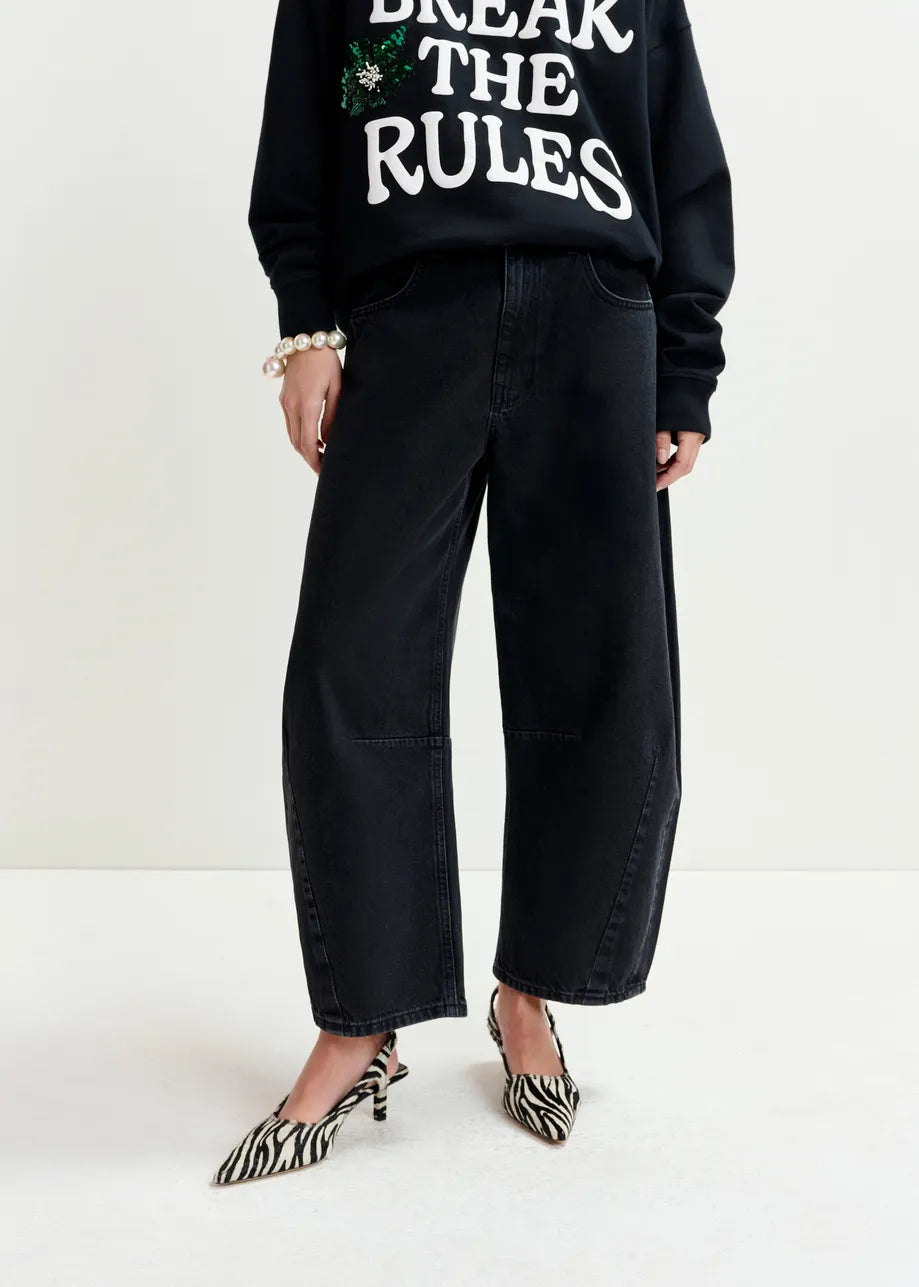 Person wearing a "Break The Rules" sweatshirt, Essentiel Antwerp Interstellar Barrel Leg Jeans in black, and zebra-print heels, standing against a plain background.