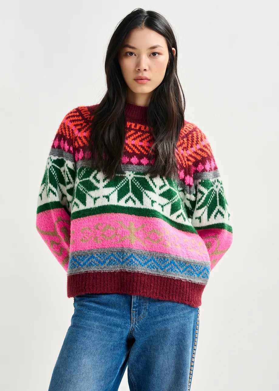 A woman wearing the Essentiel Antwerp Irelando Jacquard Knit in burgundy with blue jeans stands against a plain light background.