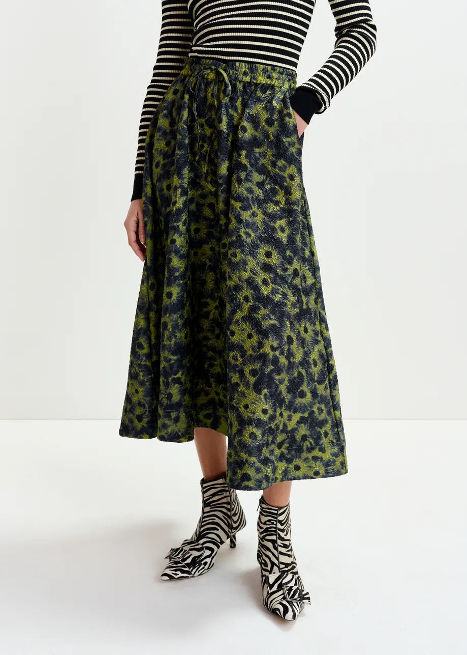 A person wearing a black and white striped long-sleeve top, zebra-print ankle boots, and the Essentiel Antwerp Isebel Floral Jacquard Skirt in khaki.