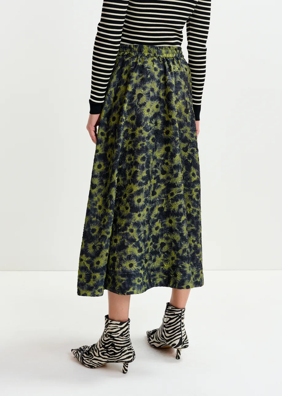 A person wears a black and white striped long-sleeve top, the Isebel Floral Jacquard Skirt in khaki by Essentiel Antwerp, and zebra-print ankle boots, standing against a plain white background.