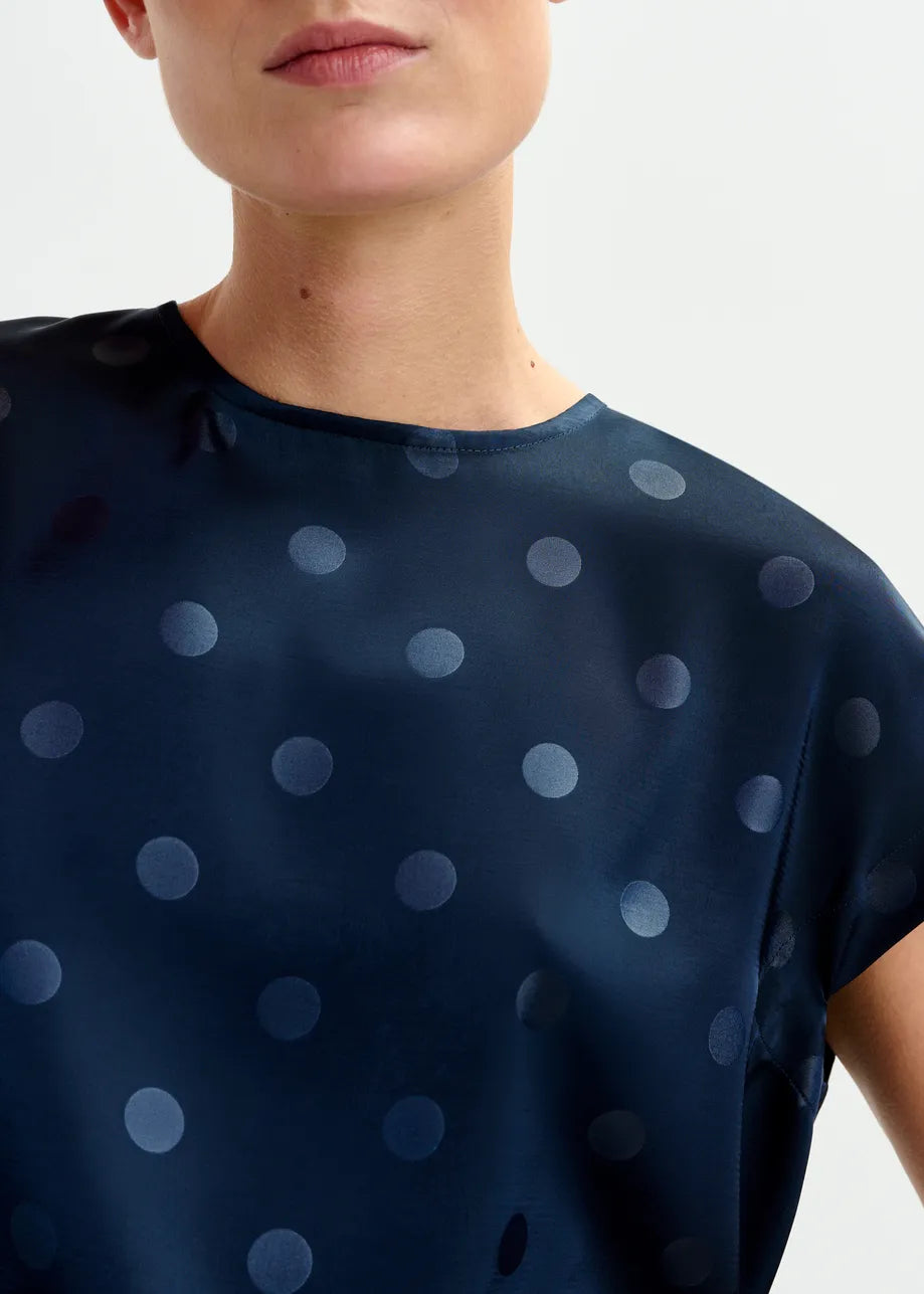 A person wears the Ishirt Polkadot Top in navy by Essentiel Antwerp, featuring cap sleeves, a relaxed fit, and polkadot pattern, shown from shoulders to upper chest.