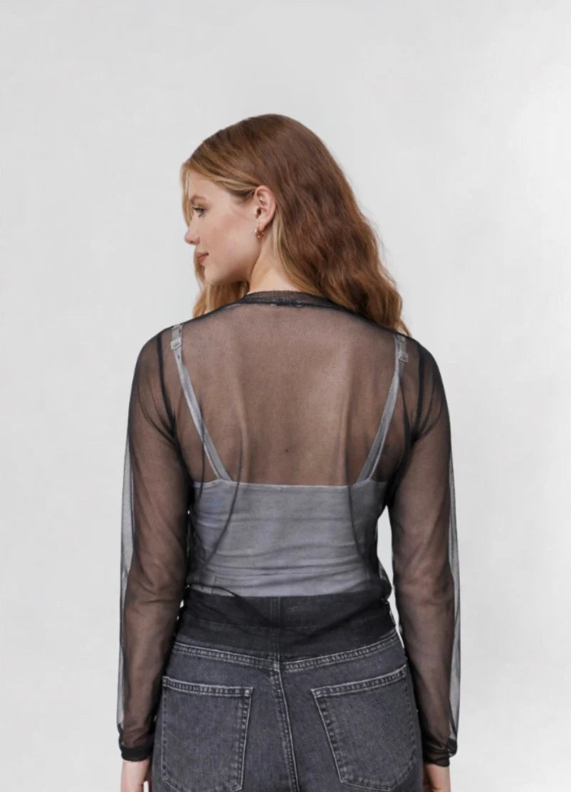 A woman with long, wavy hair is shown from the back wearing the Emin and Paul Sheer Cardigan - Black over a gray camisole and high-waisted black jeans.