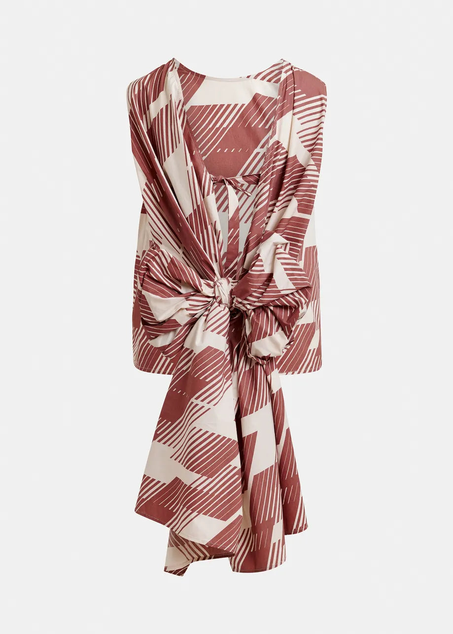 The Jelani Sleeveless Bow Top by Essentiel Antwerp features an Etruscan Red abstract geometric pattern, a prominent front bow, and a chic wrap design.