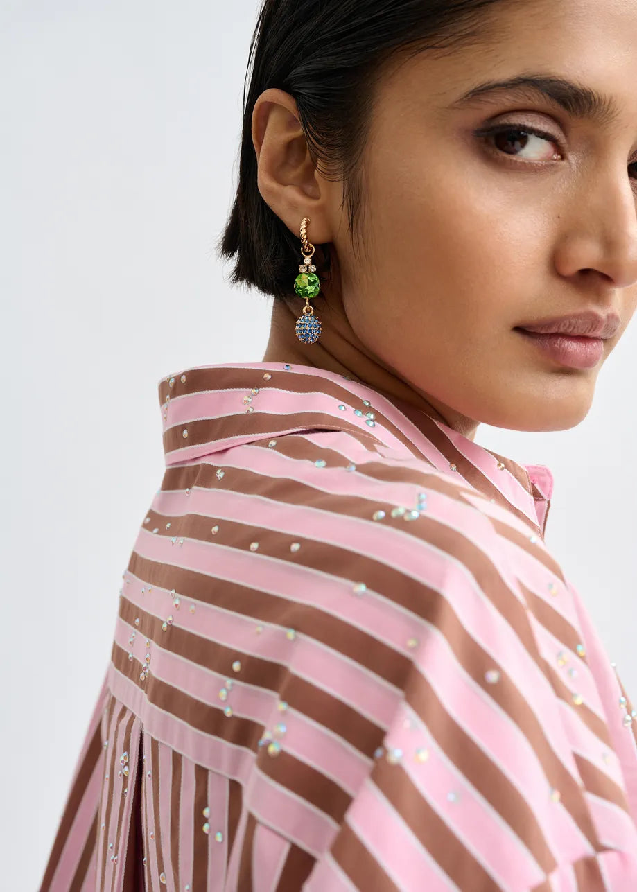A woman with short dark hair wears a pink and brown striped shirt and Essentiel Antwerp Gold Drop Earrings - Pink Dachshund, looking over her shoulder against a light background.