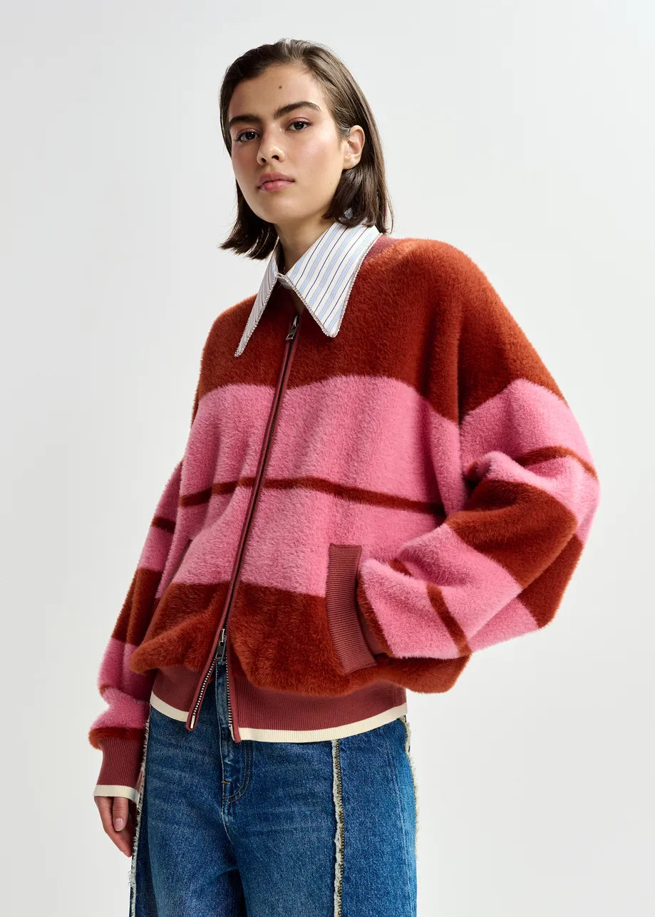 Person wearing the Essentiel Antwerp Jicama Knitted Bomber in red and pink stripes over a collared shirt and blue jeans, standing against a plain light background.