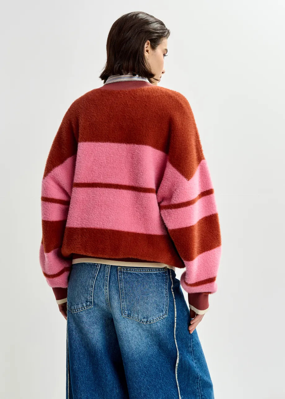 Someone wearing the Essentiel Antwerp Jicama Knitted Bomber in red and pink with blue jeans stands facing away against a plain light background.