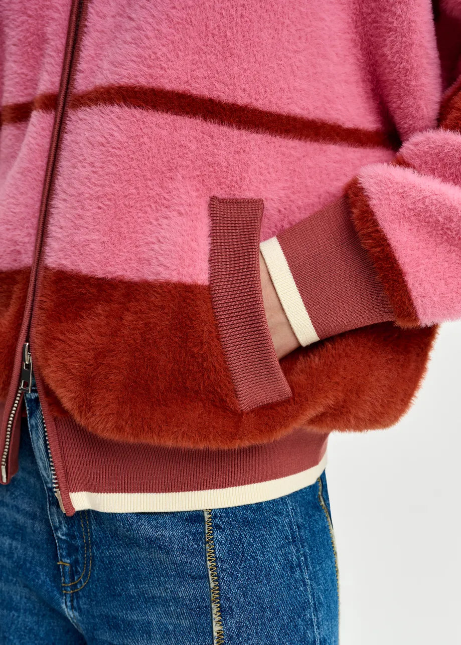 A person wears relaxed fit blue jeans and the Essentiel Antwerp Jicama Knitted Bomber in red and pink, with one hand in the pocket.