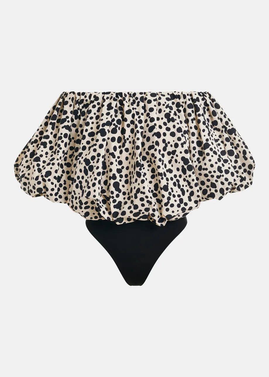 The Essentiel Antwerp Jint Puff Sleeve Bodysuit in black & white pairs a bold off-shoulder, polka dot ruffled top with a sleek solid black bottom for a standout modern look.