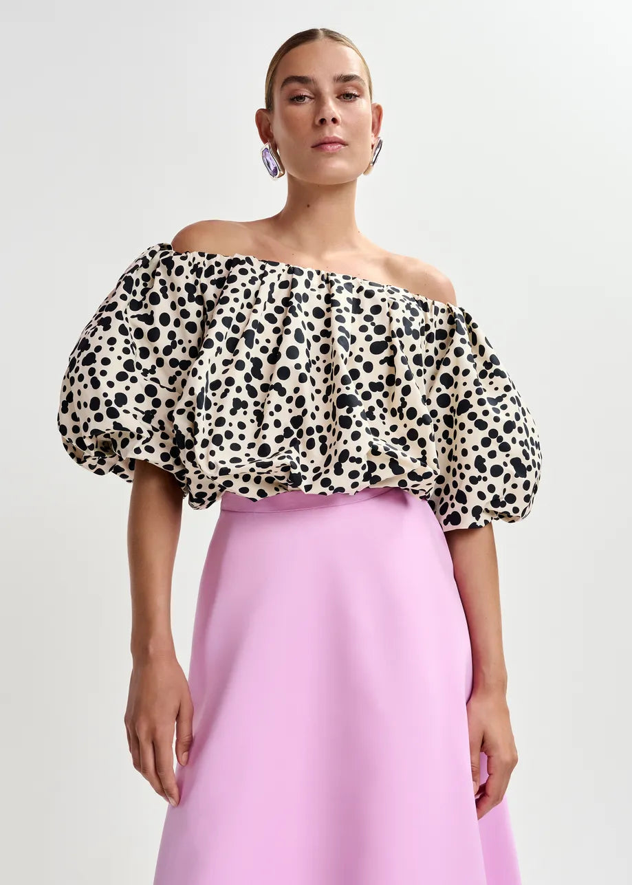 A person wears the Essentiel Antwerp Jint Puff Sleeve Bodysuit in black & white, styled with a high-waisted light pink skirt.