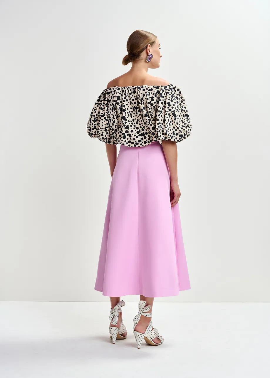 A woman in a pink high-waisted skirt and the Essentiel Antwerp Jint Puff Sleeve Bodysuit in black & white.
