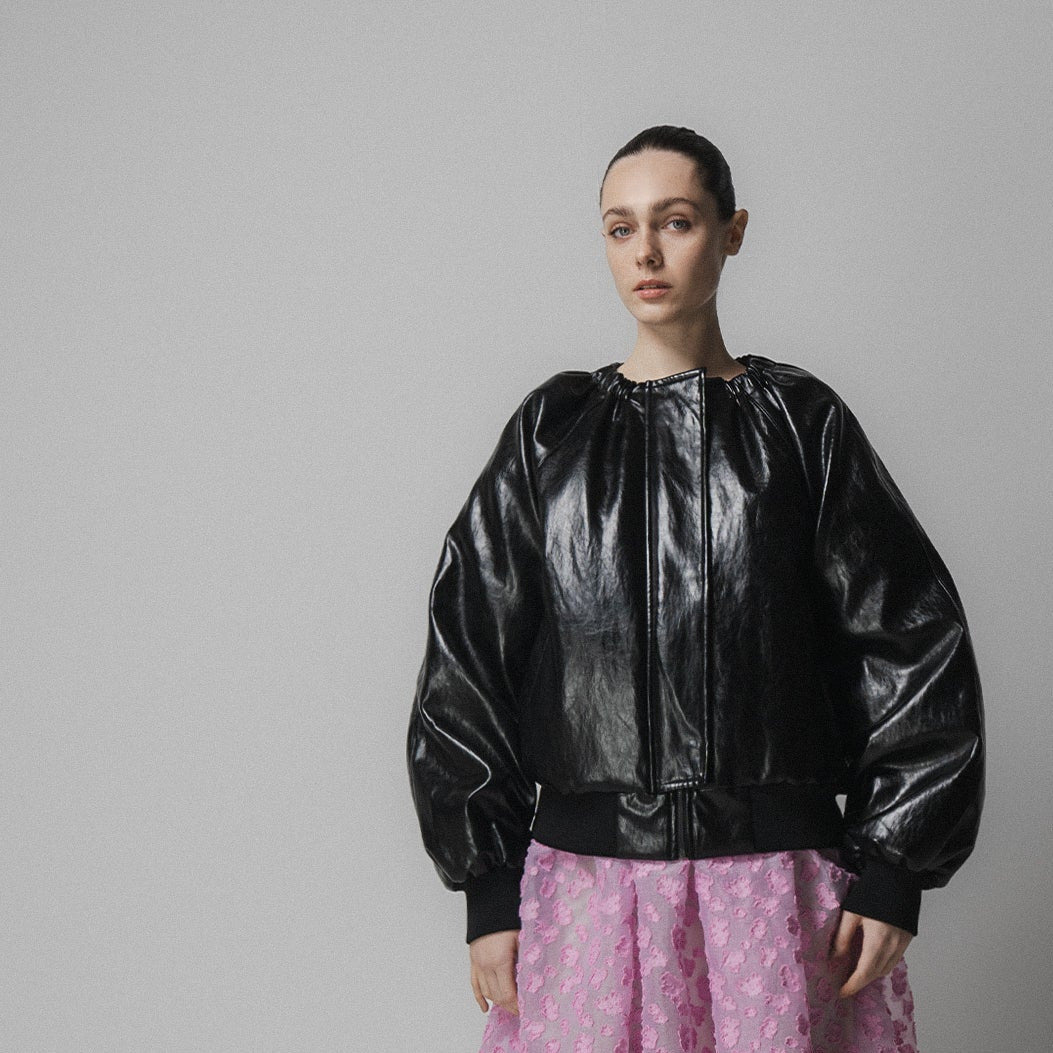 woman wears emin and paul black leather jacket with a pink skirt and grey tights and black shoes on a grey background