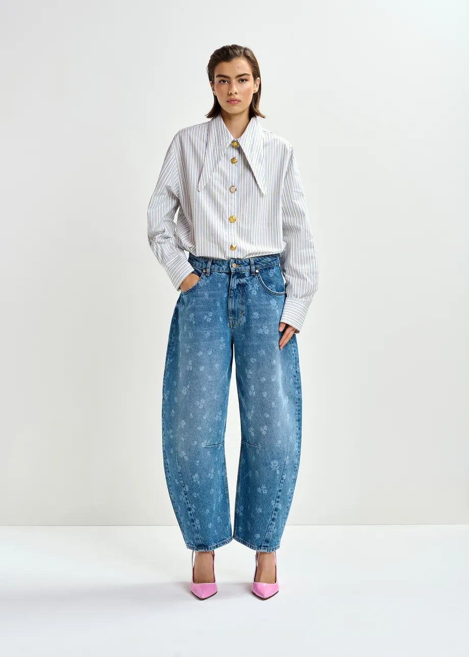 A person stands against a white background wearing Essentiel Antwerp's Jo1 Barrel Cropped Jeans in Blue Floral.
