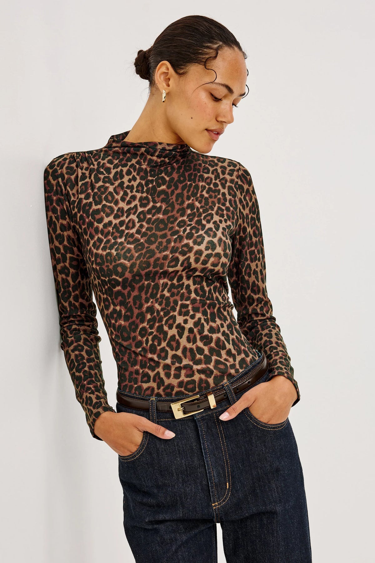 A person wearing a Rails Joelle Top - Brown Nala, a long-sleeved, funnel neckline mesh top with a brown and black leopard print, tucked into dark denim jeans with a brown leather belt.