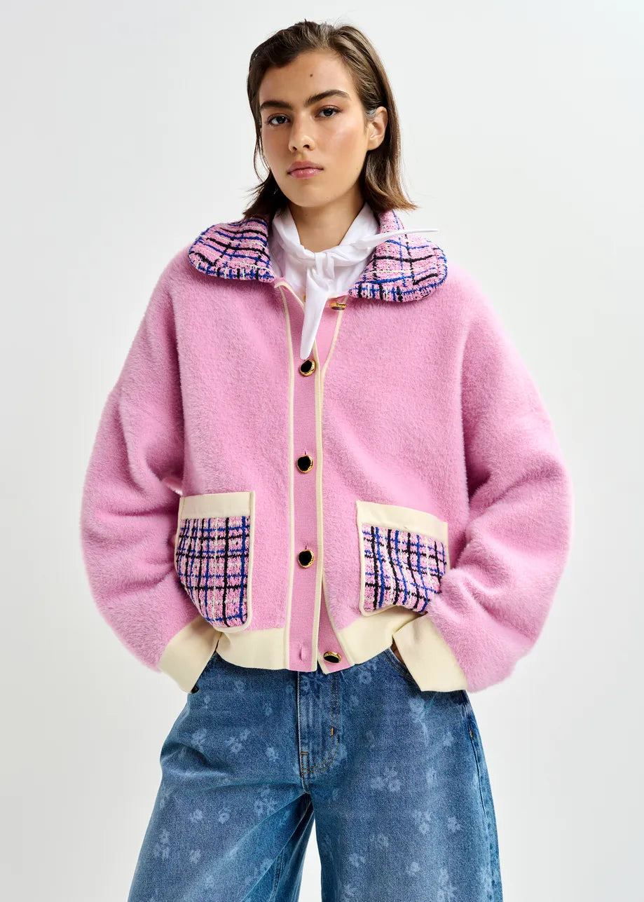 A person wears the Essentiel Antwerp Joilu Contrast Knit Cardigan in pink, featuring plaid collar and pocket details, paired with loose blue jeans, standing against a plain white background.