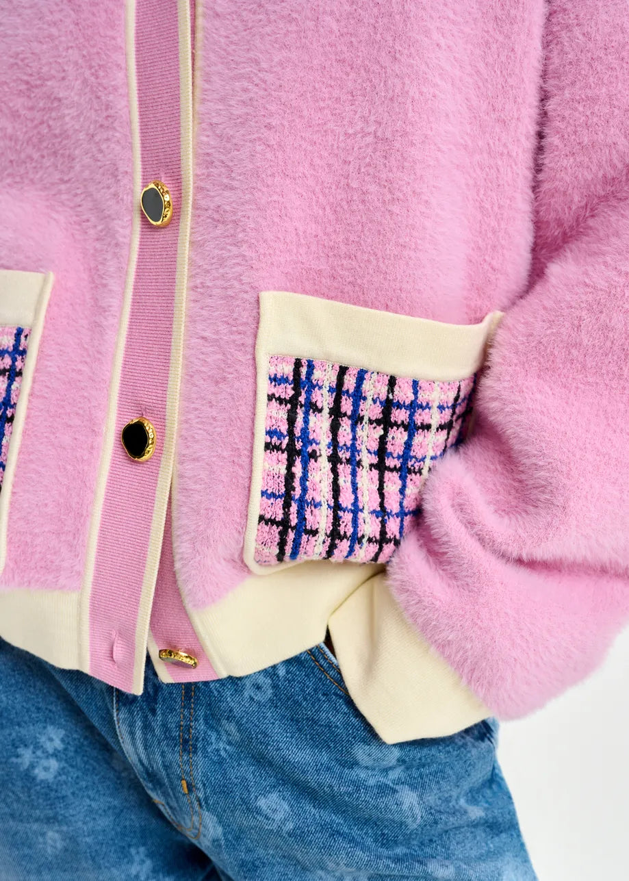 A person wears the Essentiel Antwerp Joilu Contrast Knit Cardigan in pink, featuring a relaxed fit and patterned pockets with gold buttons, paired with blue jeans.