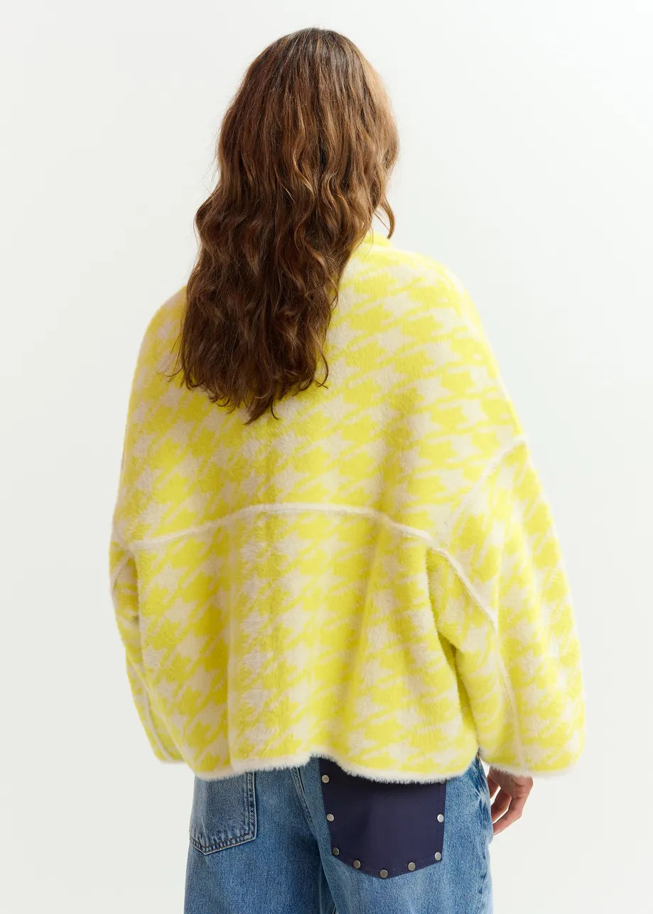 Person with long wavy hair, facing away from the camera, wears blue jeans and the Essentiel Antwerp Joking Houndstooth Knit Cardigan in yellow.