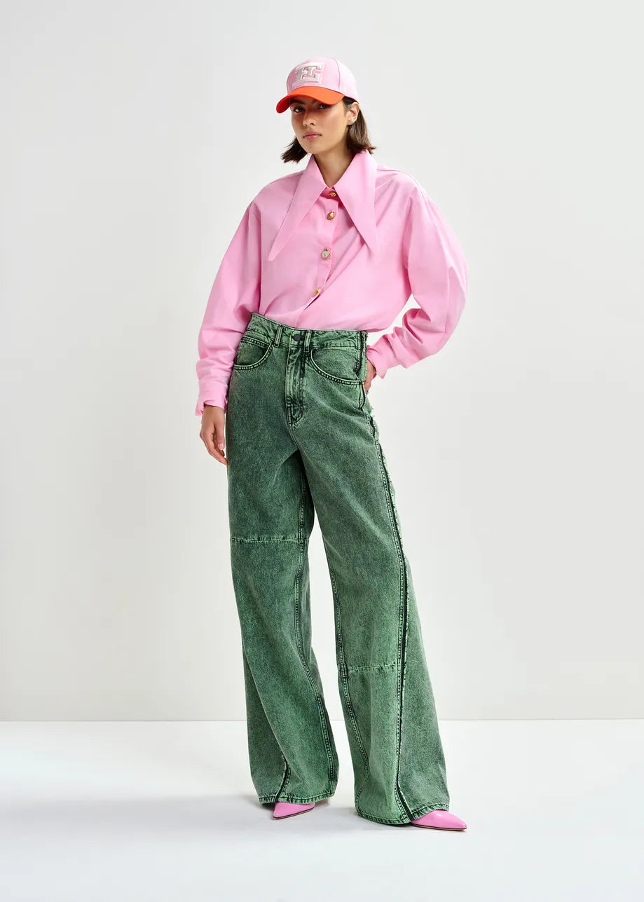 A person wearing the Essentiel Antwerp Jomato Pointed Collar Shirt in pink, green wide-leg jeans, pink shoes, and a pink baseball cap stands against a plain light background.