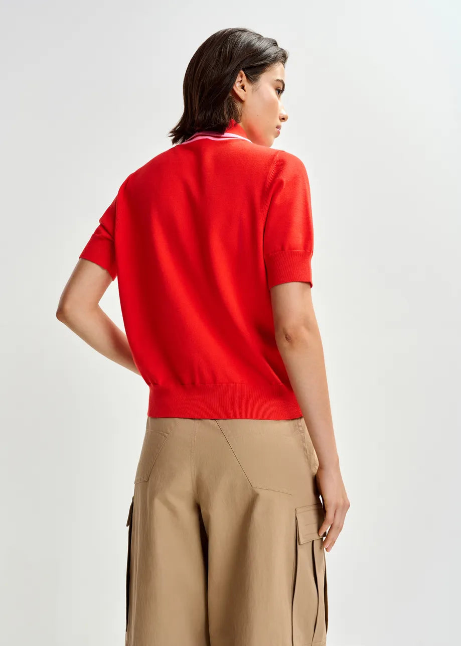 A person stands with their back to the camera, wearing the Essentiel Antwerp Jonda Knit Polo in red/light pink and beige cargo shorts against a plain light background.