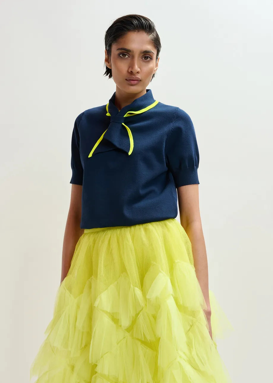 A woman in a yellow skirt styles her outfit with the Essentiel Antwerp Jonda Knit Polo in navy/neon yellow, creating a chic and effortless look for any occasion.