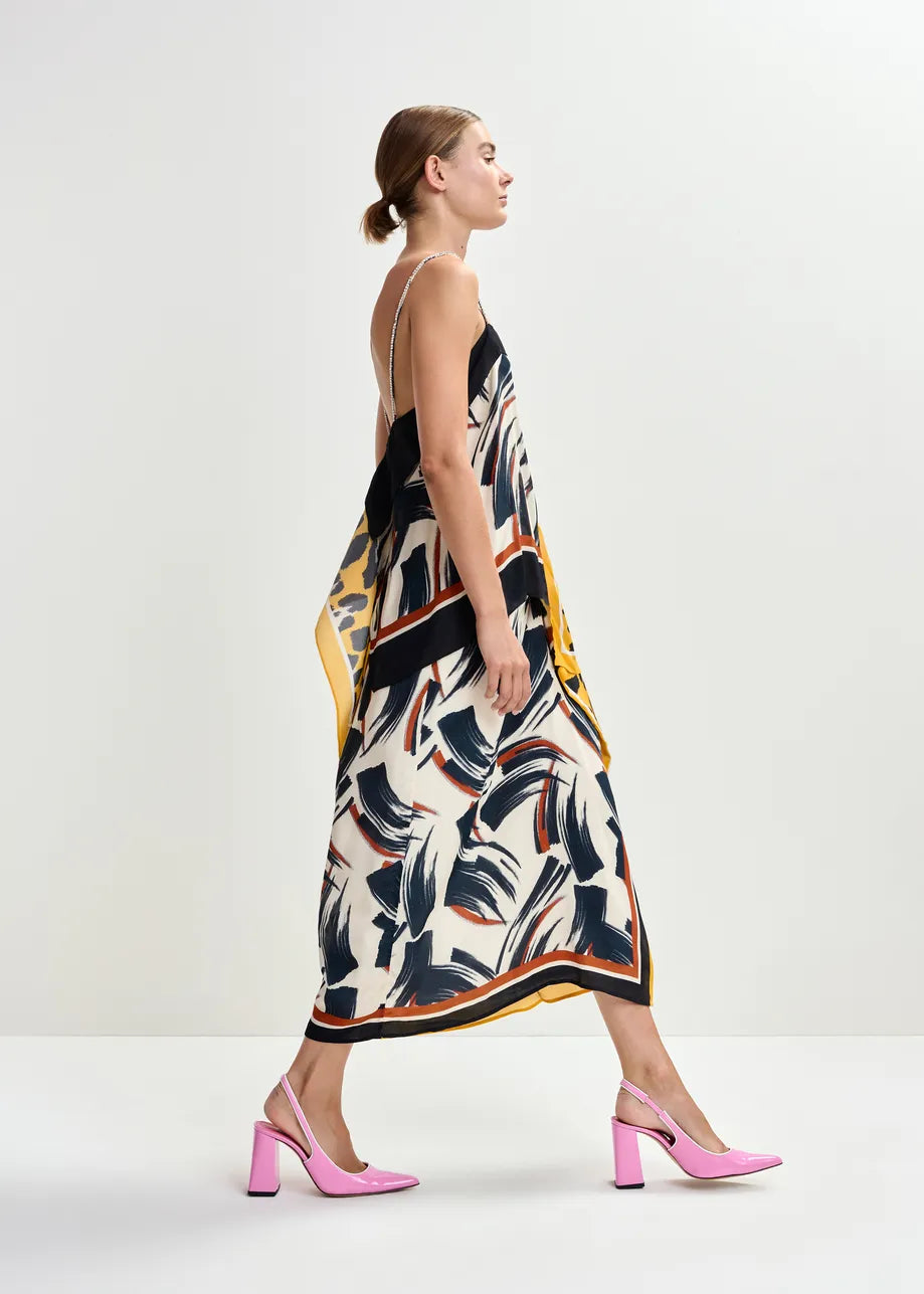 A woman in the Essentiel Antwerp Juanita Drape Midi Skirt in ochre, styled with pink heels, walks in profile against a plain white background.