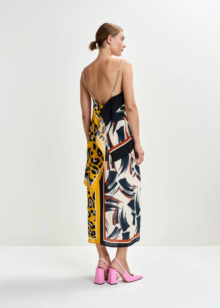 Woman stands against a plain backdrop wearing the Essentiel Antwerp Josette Two Print Slip Top, featuring a brushstroke design and gemstone-embellished straps. She's seen from behind in pink block-heeled shoes.