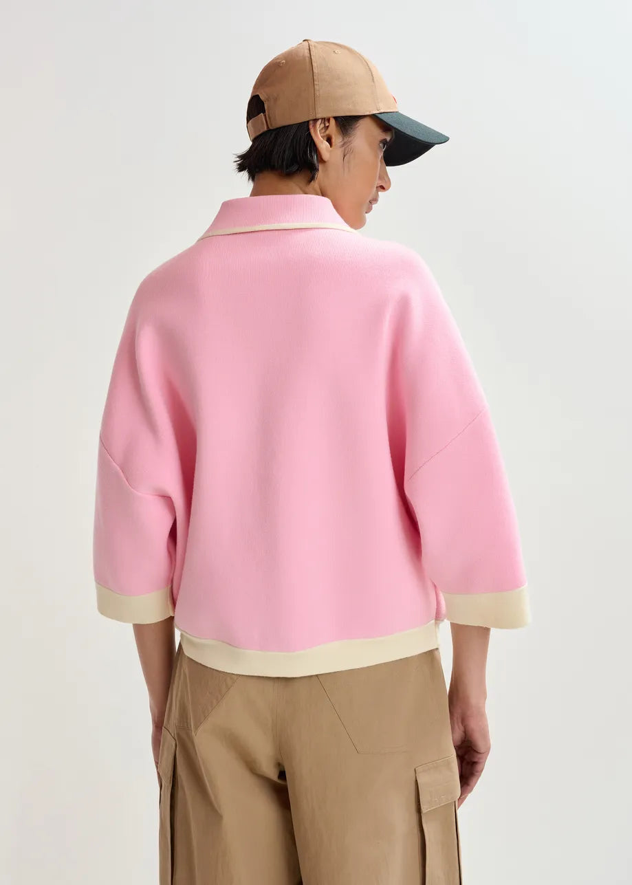 A person stands with their back to the camera against a plain background, wearing a tan baseball cap, tan cargo pants, and the Essentiel Antwerp Jugly Contrast Knit Cardigan in pink.