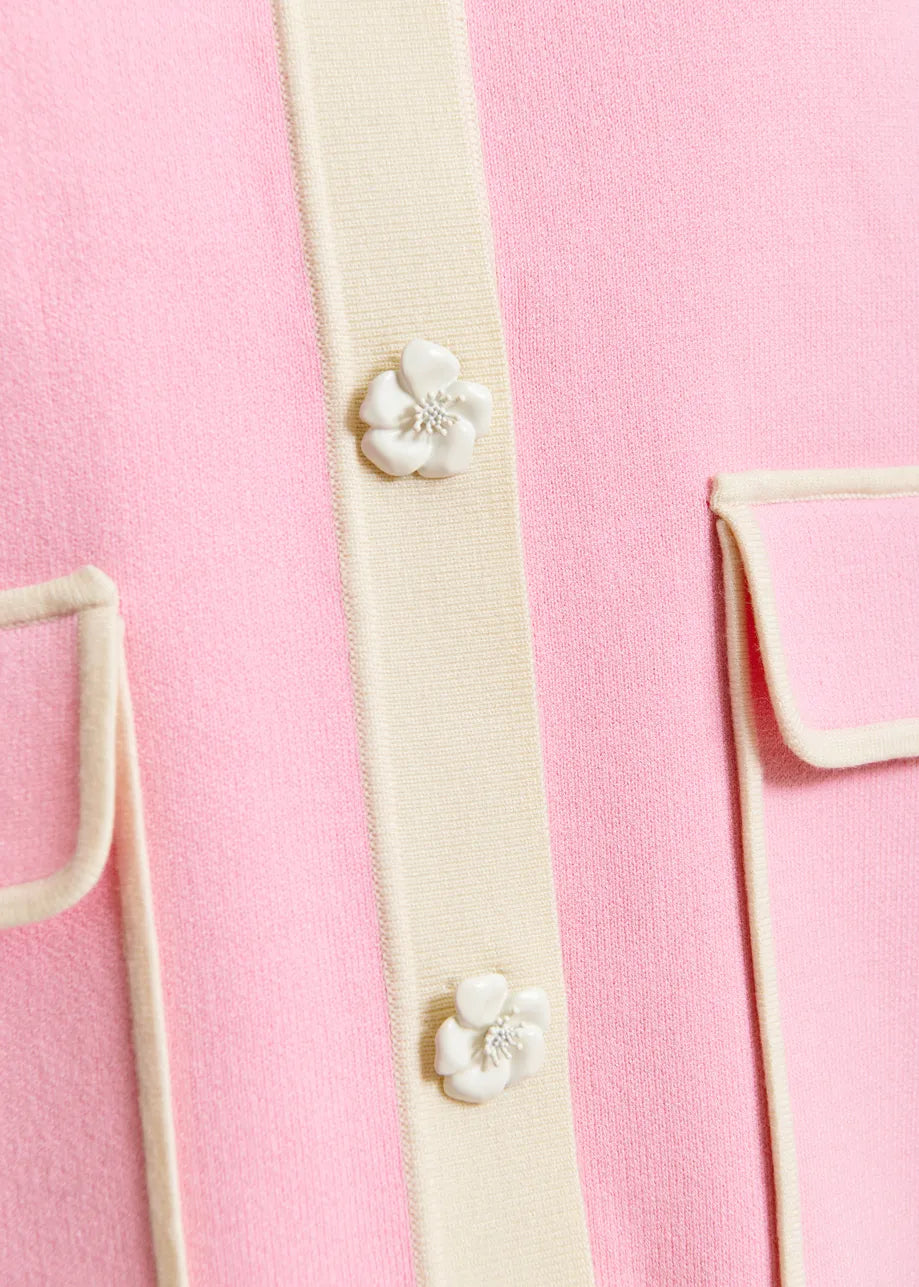 Close-up of the Jugly Contrast Knit Cardigan in pink by Essentiel Antwerp, featuring cream trim, two white flower snap buttons, and two flap pockets.