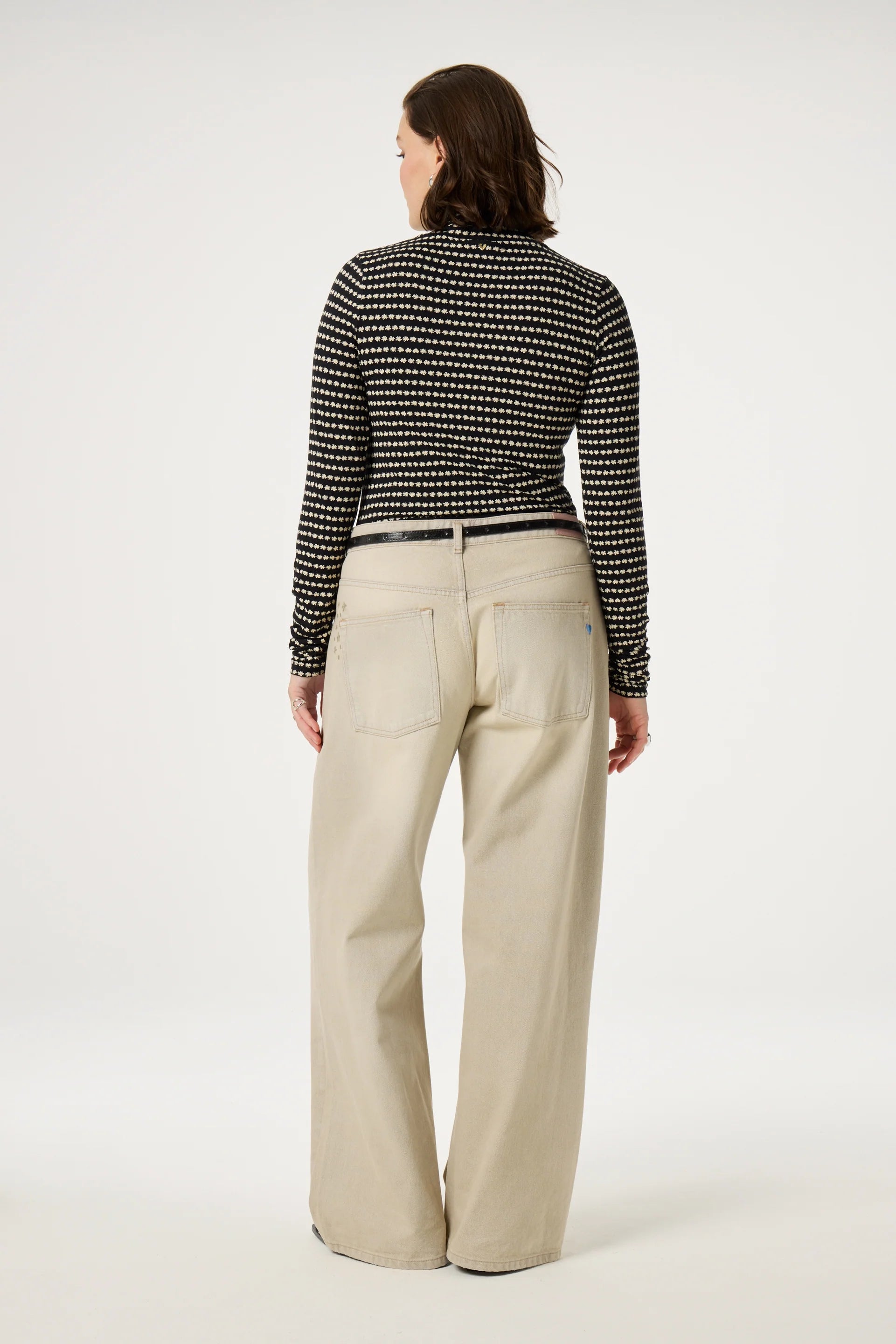 A person wearing the Jade Top - Black by Fabienne Chapot and beige wide-leg pants stands facing away.