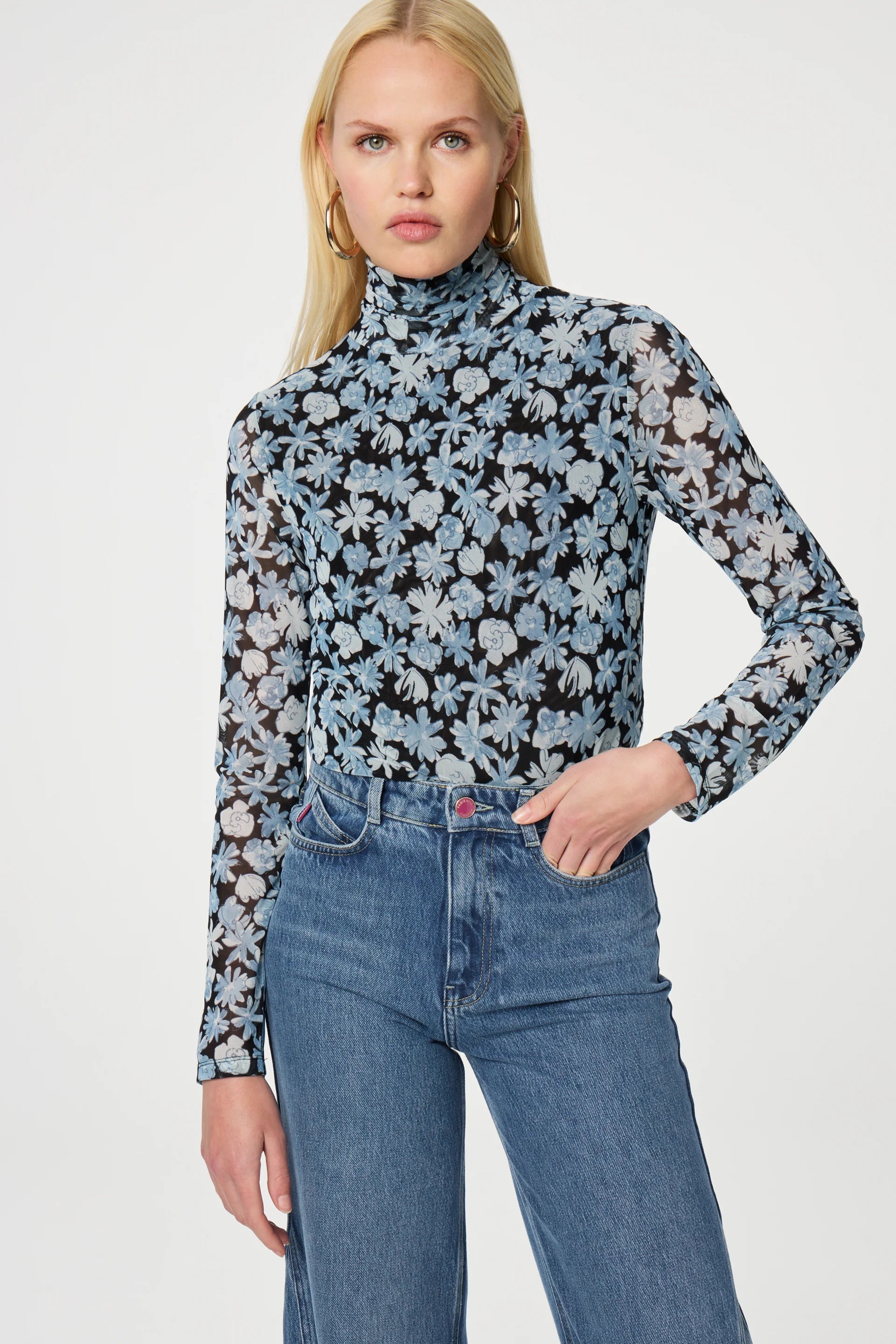 A person wearing the Jane Top - Blue Freja by Fabienne Chapot and jeans stands against a plain background.