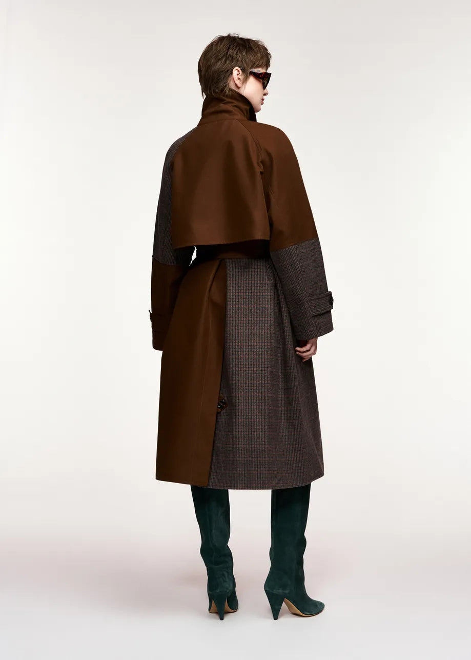 A model shown from the back wearing a long brown and dark gray coat with a high collar, dark green knee-high boots, and sunglasses, set against a plain light gray studio background.