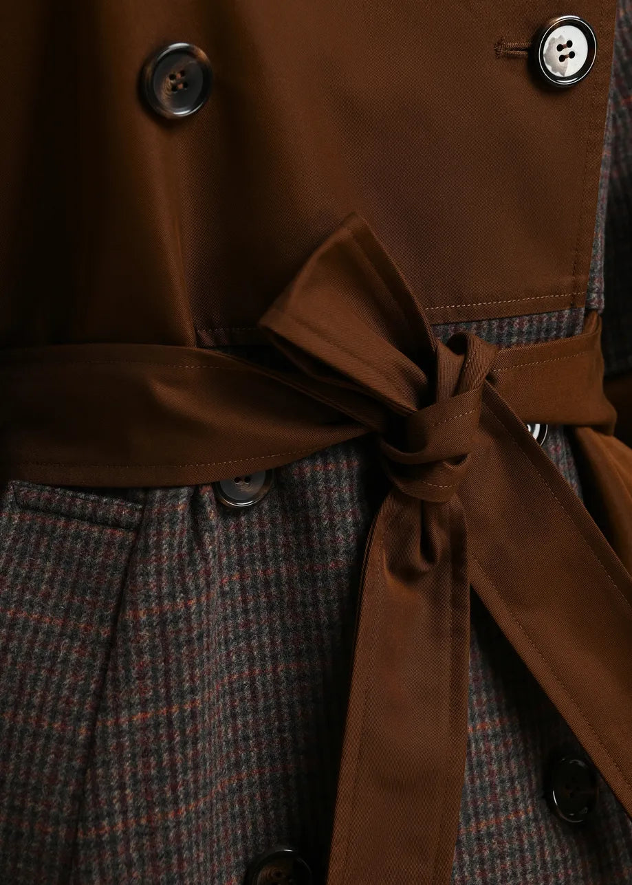 Close-up of a double-breasted coat with a brown satin-like waist tie and a brown-and-gray houndstooth patterned body, showing dark buttons. essentiel antwerp