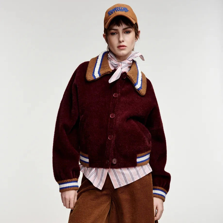 A model wearing a dark burgundy corduroy button-up cardigan with a striped and brown patterned collar, layered over a striped shirt and brown wide-leg corduroy pants, paired with a brown cap.