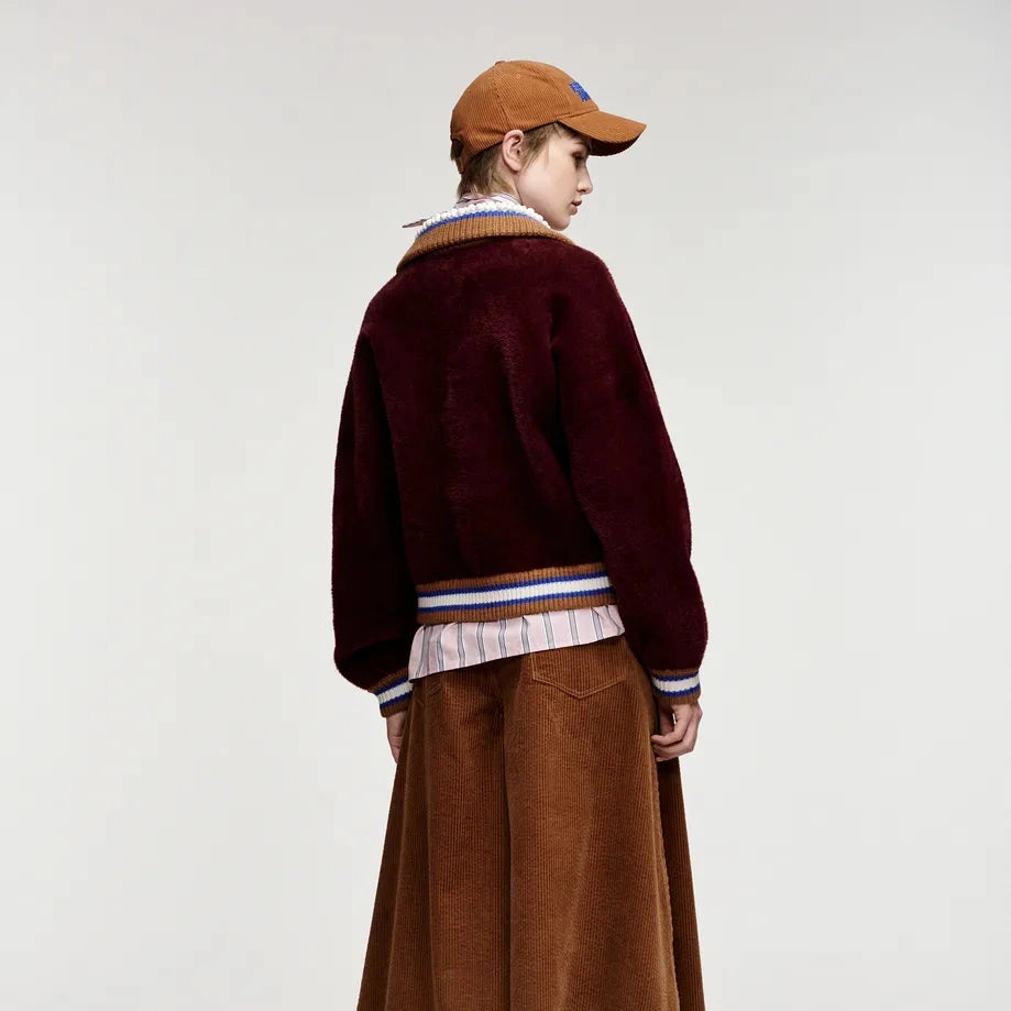 A model shown from the back wearing a dark burgundy fuzzy cropped cardigan over a striped shirt, a brown corduroy skirt, and black knee-high boots, against a plain light gray studio background.